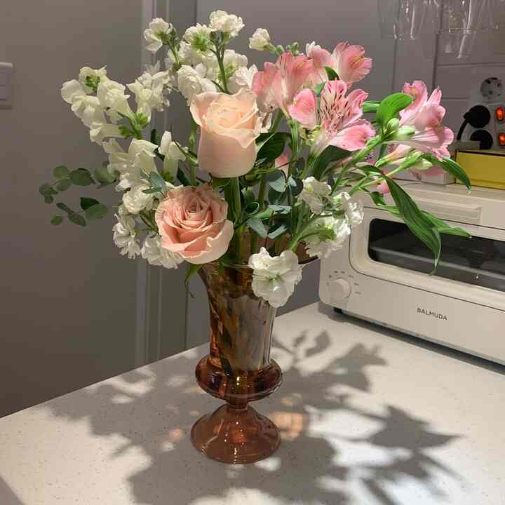 Soft pastel-colored flowers arranged in a brown vase on a kitchen countertop