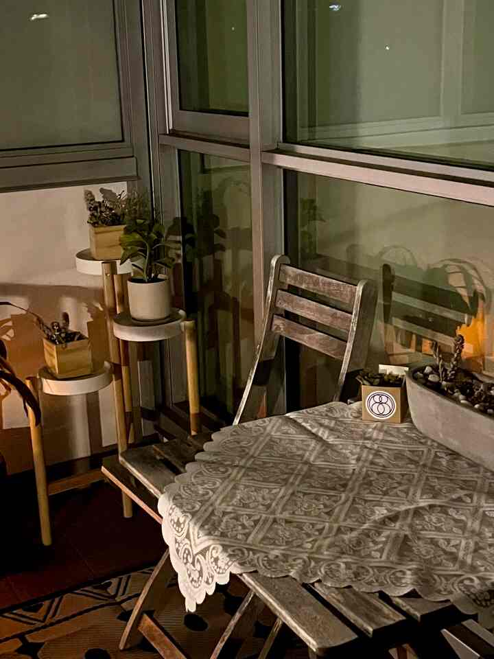 Beige and brown toned balcony space featuring wooden outdoor table and chair with plant stands, creating a cozy atmosphere