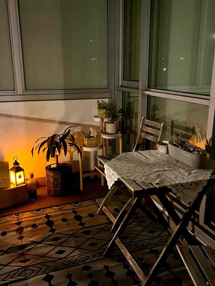 Brown and beige toned balcony space featuring wood table and chairs with lace tablecloth and cozy lantern lighting in a natural atmosphere