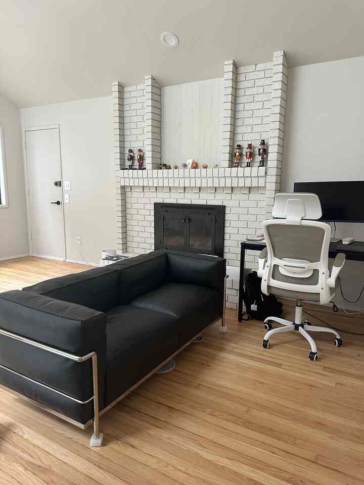 Modern living room with black sofa and white office chair, featuring a central white brick fireplace creating cozy atmosphere