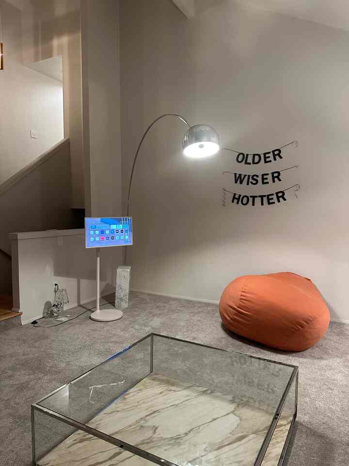 Gray-toned living room with an orange bean bag, glass marble coffee table, and modern floor lamp creating a simple, cozy space
