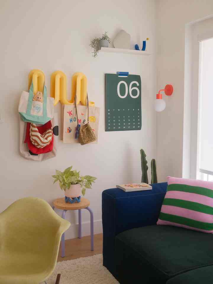 Bright white walls with a navy sofa, yellow chair, yellow wall-mounted storage, green plants, and a calendar in a warm cozy living room