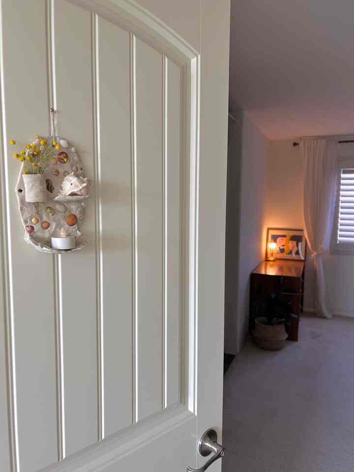 Bright white-toned entrance door with beige décor seen into a natural living space, featuring a desk with warm lighting creating a cozy atmosphere