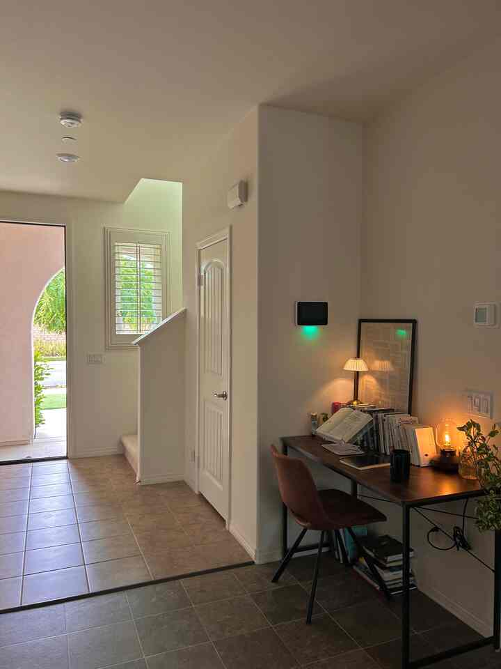 White-walled entrance area featuring a cozy home office setup with desk and table lamp on the right