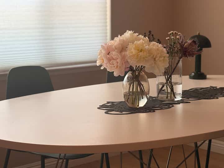 Soft beige and white toned dining space featuring vases with flowers and subtle lighting creating a cozy atmosphere