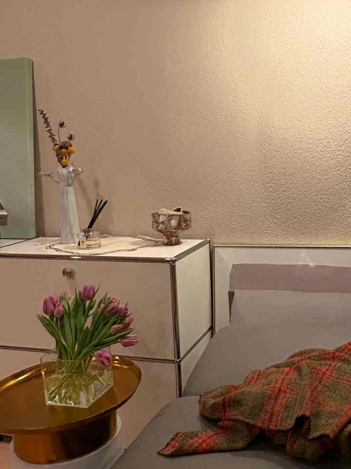 Natural beige-toned bedroom featuring a gray bed and white sideboard adorned with flowers and diffuser, creating a cozy atmosphere