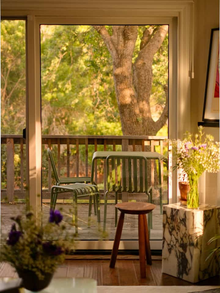 Warm wood tones and transparent glass doors reveal a balcony space featuring a green outdoor table set and marble plinth, creating a nature-inspired atmosphere