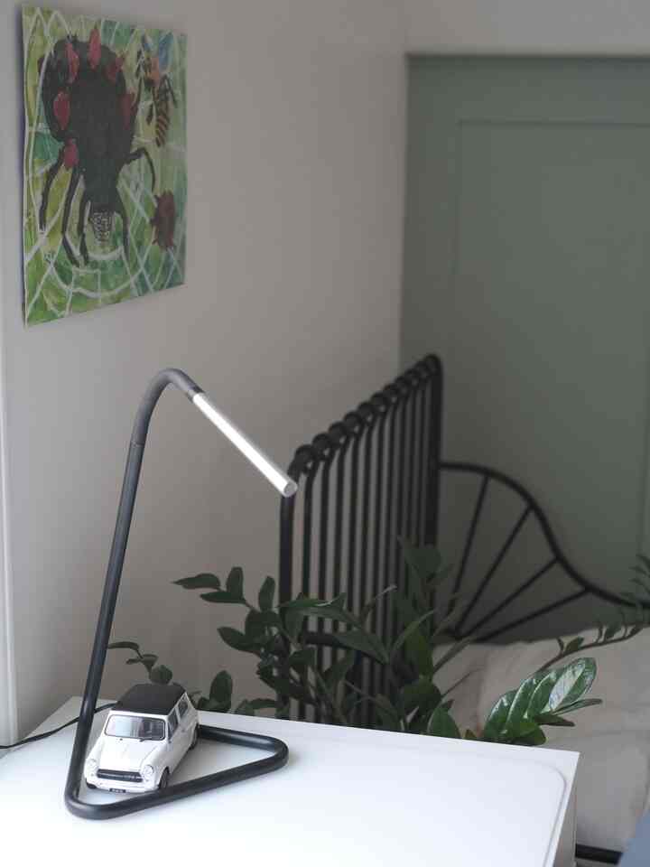White and black toned kids' room featuring a white desk with an IKEA adjustable LED desk lamp and miniature car model, cozy space with black metal bed frame and greenery