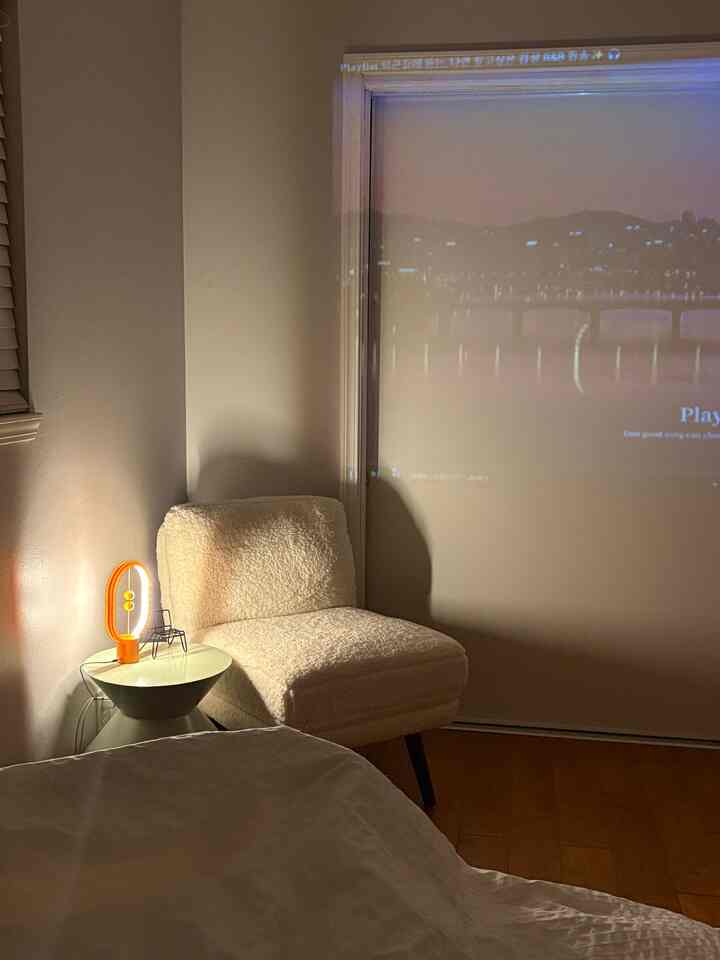 A cozy living room corner in white and green tones featuring a soft textured chair and an orange table lamp