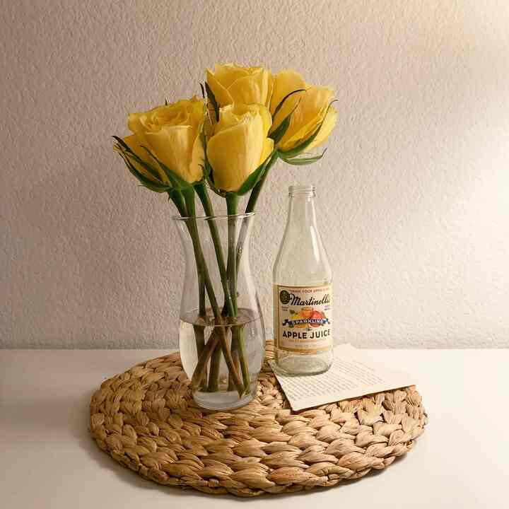 Yellow-toned natural color table setting with transparent vase holding yellow roses and a clear bottle