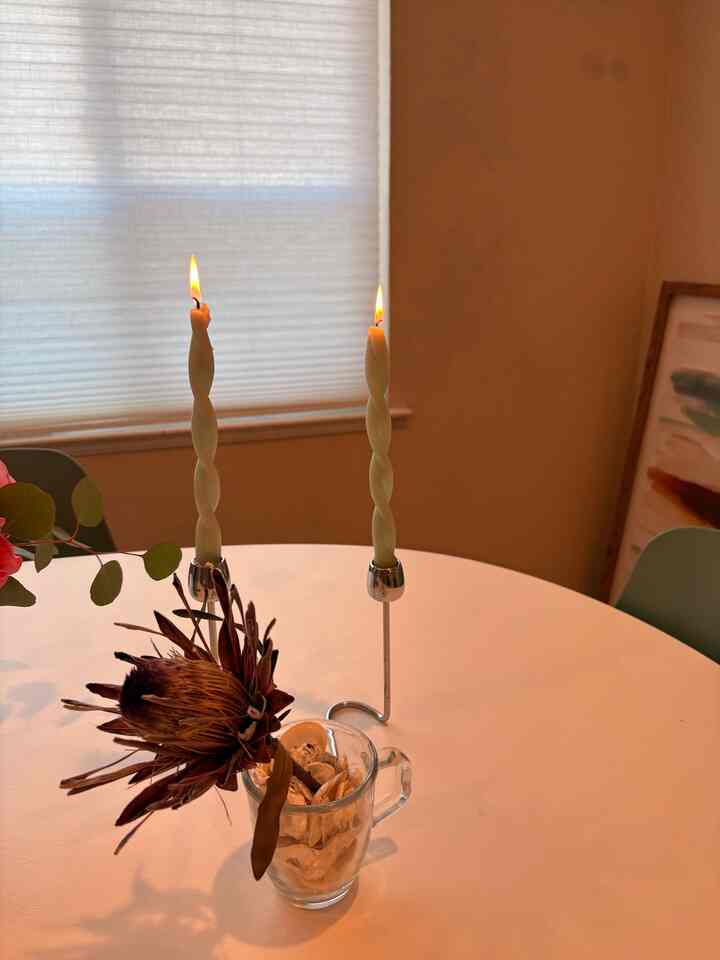 White and brown toned dining room featuring two lit candles on a round dining table with natural dried flower decor, creating a cozy atmosphere