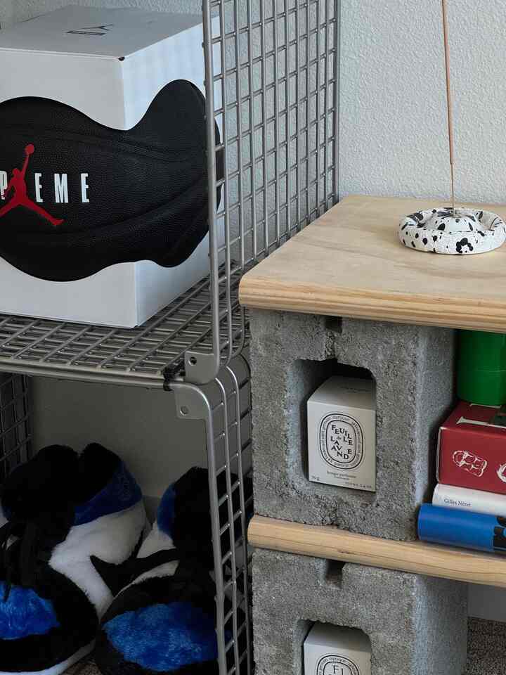 Minimal interior featuring blue and black sneakers beside concrete shelving displaying Diptyque lavender candles and incense holder
