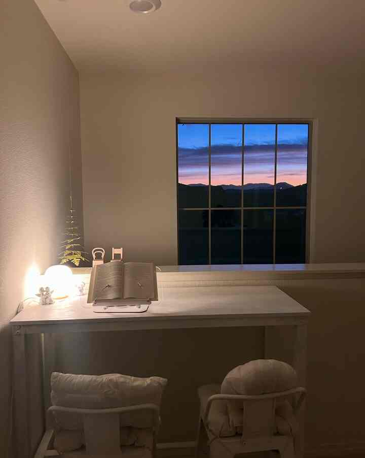 White and beige toned small meditation space featuring desk, stools, and warm table lamp in a cozy corner
