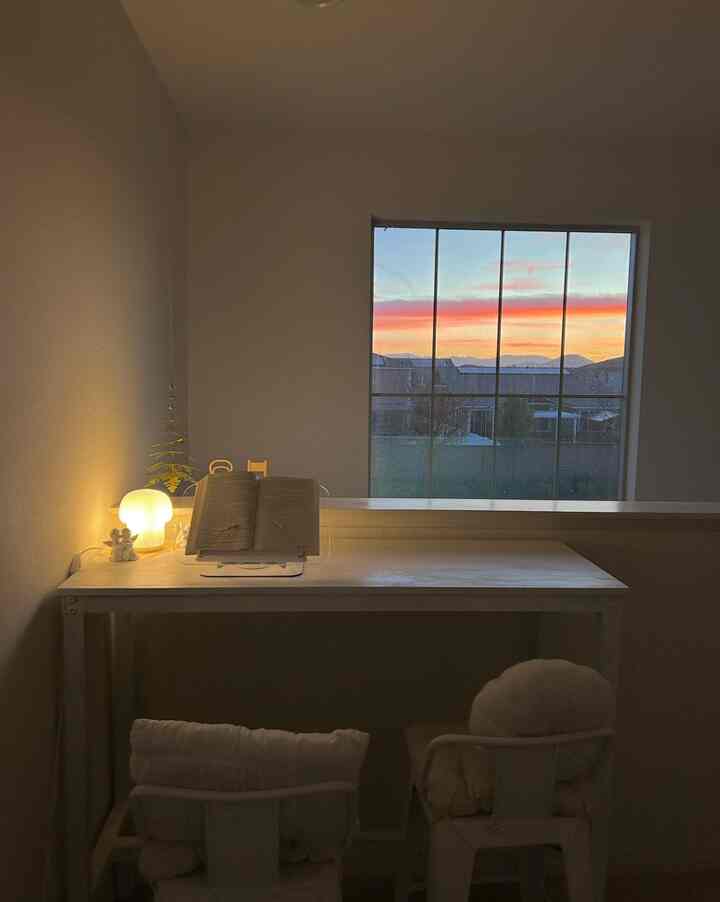 Warmly lit small nook with white tones, featuring a desk with a book and lamp, creating a cozy meditation space