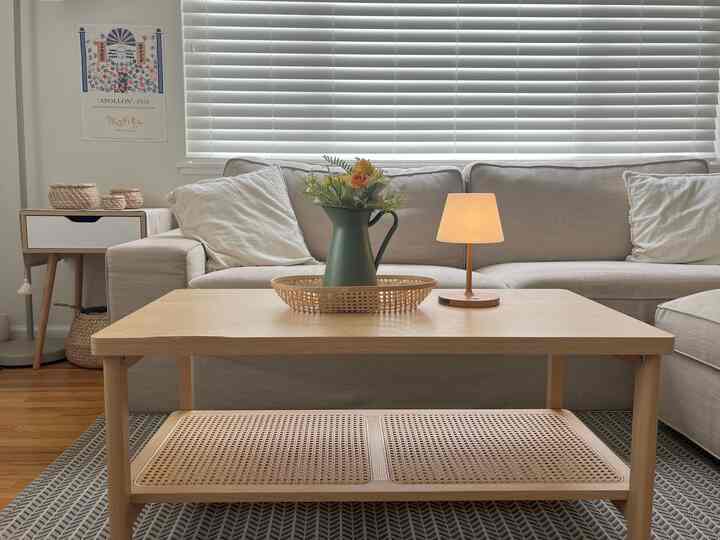 Natural and white toned living room featuring beige sofa, wooden coffee table with vase and table lamp, creating a cozy atmosphere
