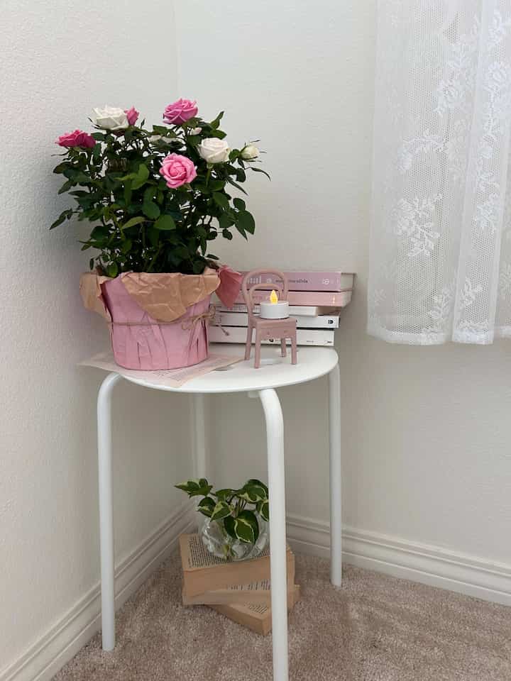 White and pink toned corner space featuring plants and a small decorative light on a simple cozy table