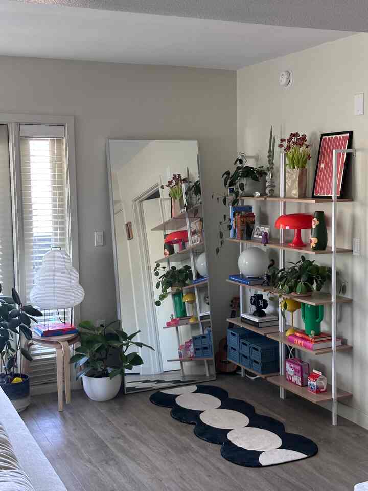 White and wood tone living room featuring a large mirror, shelves with plants and decor, and a patterned rug in a modern natural atmosphere