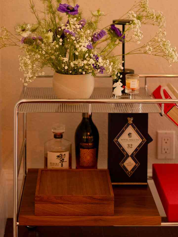 Cozy corner featuring a brown and silver bar cart topped with a vase of flowers and a candle