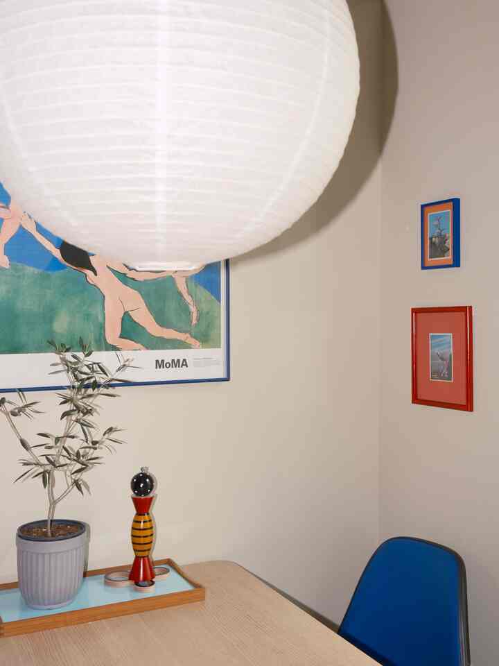 Natural-toned dining room featuring vintage posters and postcard frames on the wall, with a wooden table holding vintage objects and a plant creating a cozy atmosphere