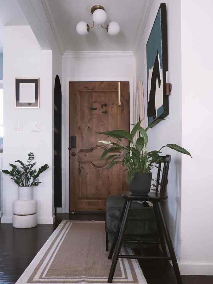 Natural modern entrance space with white walls and wooden door, featuring wood furniture and green plants for a calm, neat atmosphere
