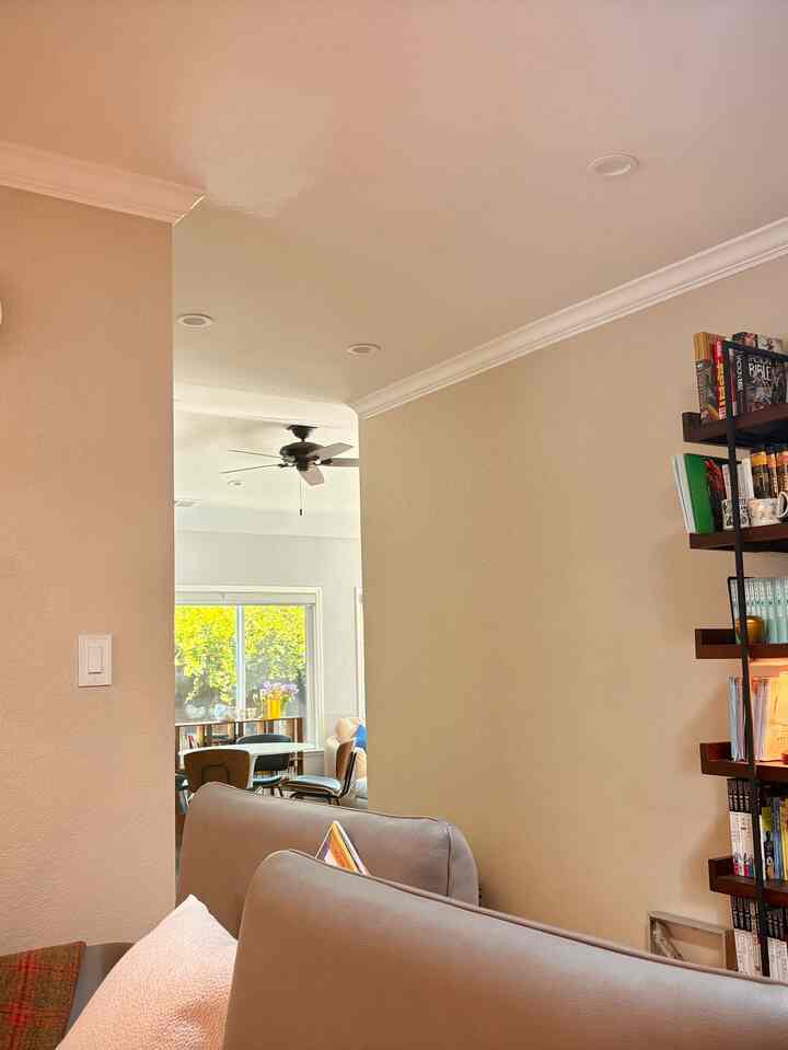 Beige-toned living room with wood-tone bookshelf, grey sofas positioned foreground creating cozy reading corner