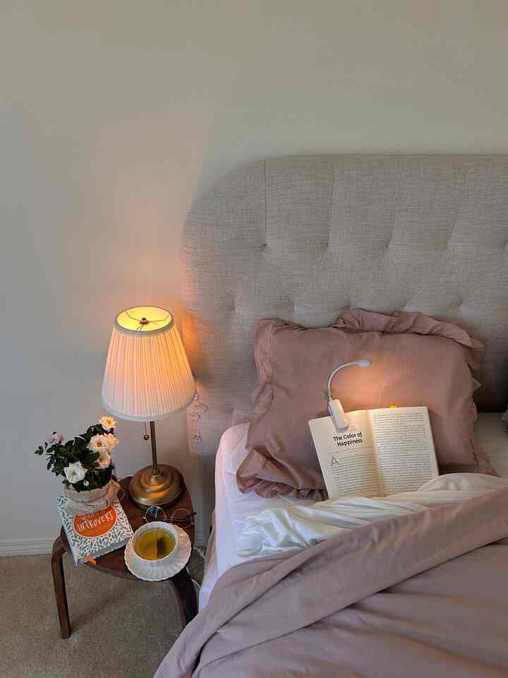 Soft white and light gray toned bedroom featuring brown nightstand, table lamp, and pink bedspread creating cozy atmosphere