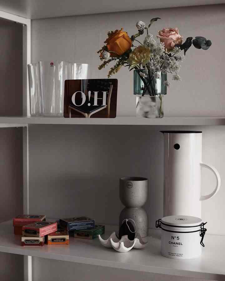 White and natural tone shelves featuring a vase with flowers, vacuum jug, and small accessories in a minimal setting