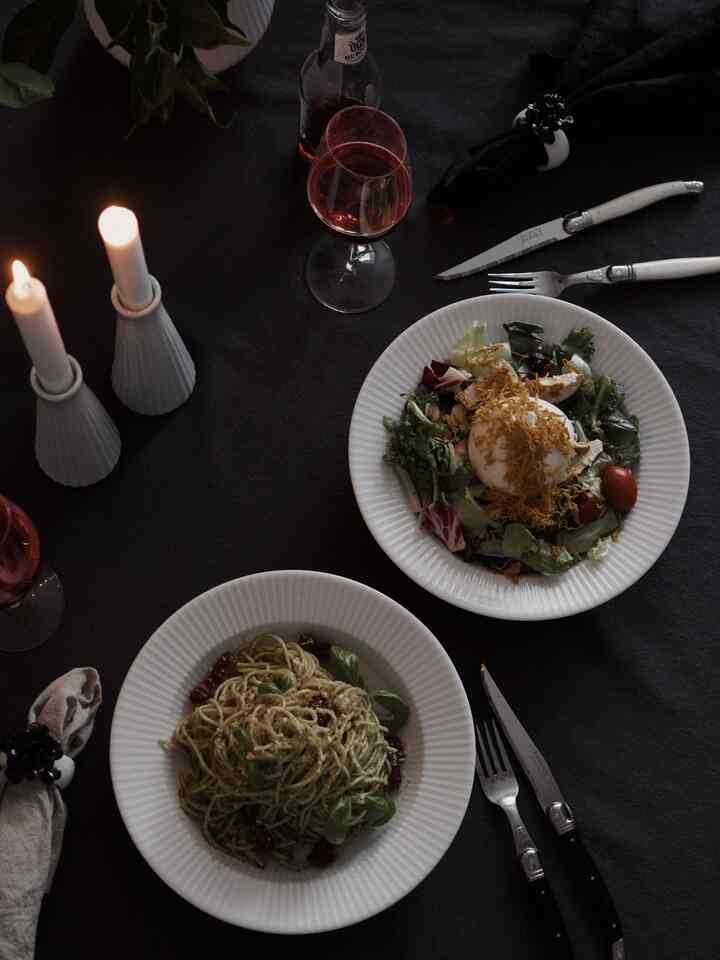 A simple and modern dining room for four featuring white plates, candles, and wine glasses on a dark black tablecloth for dinnertime
