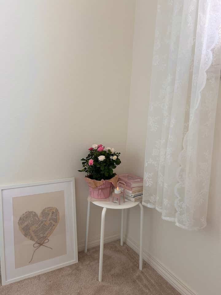 Cozy small room corner in white and beige tones, with a white side table featuring flowers and books