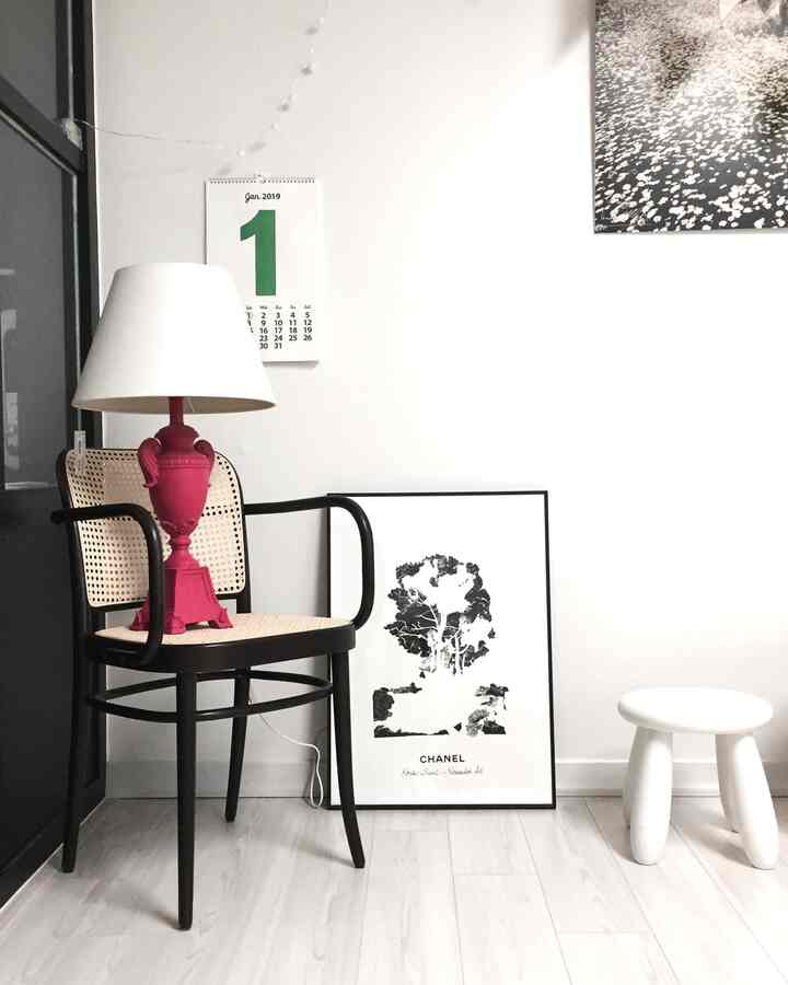 Minimal living room corner in white and black tones featuring an armchair, stool, and red table lamp with a clean, modern vibe