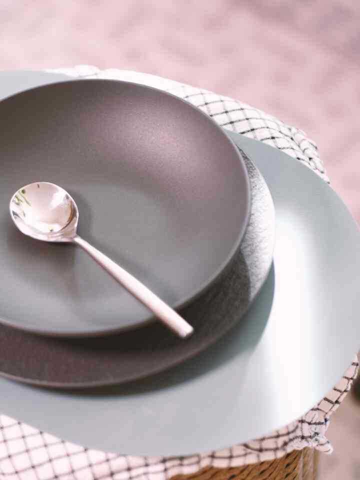 Simple table setting featuring plates, bowl, and silver spoon on soft gray and light blue toned tablecloth