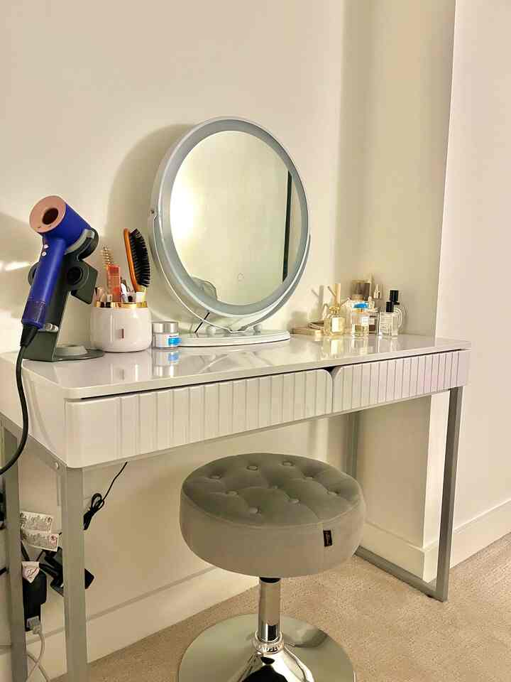 Minimalist vanity space in white and silver tones, featuring a round mirror and stool with a clean modern interior design