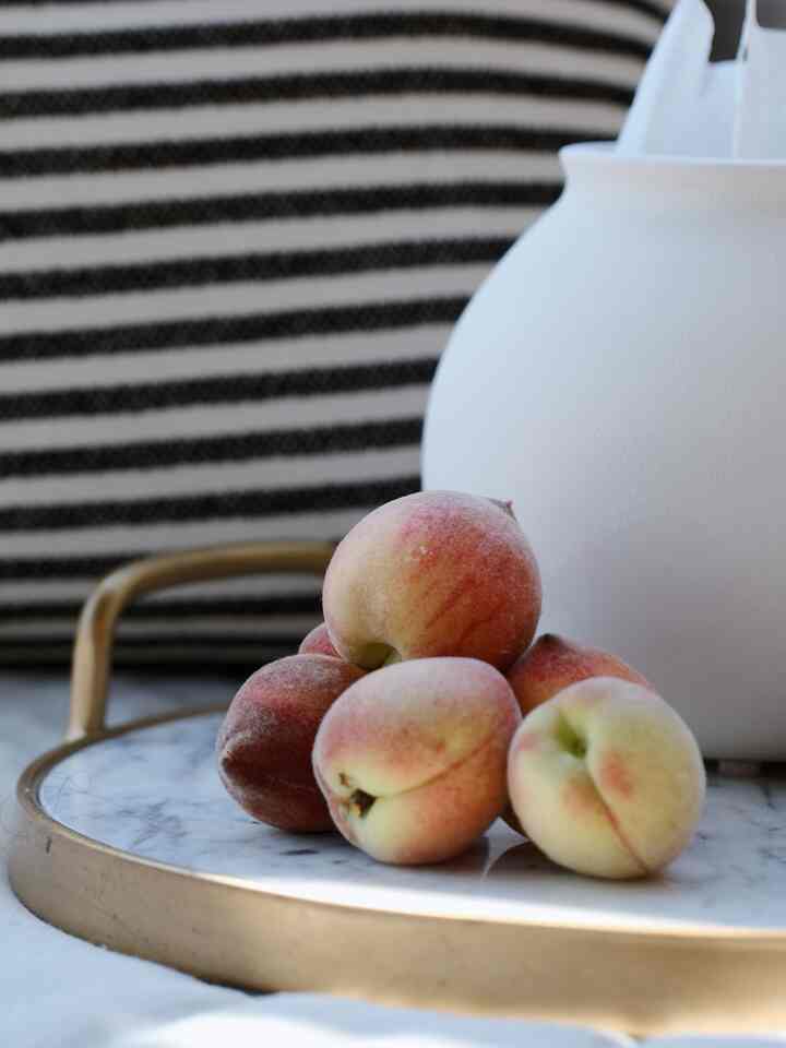 Simple and elegant interior decor featuring a white ceramic vase and gold-rimmed marble tray with peaches arranged on top