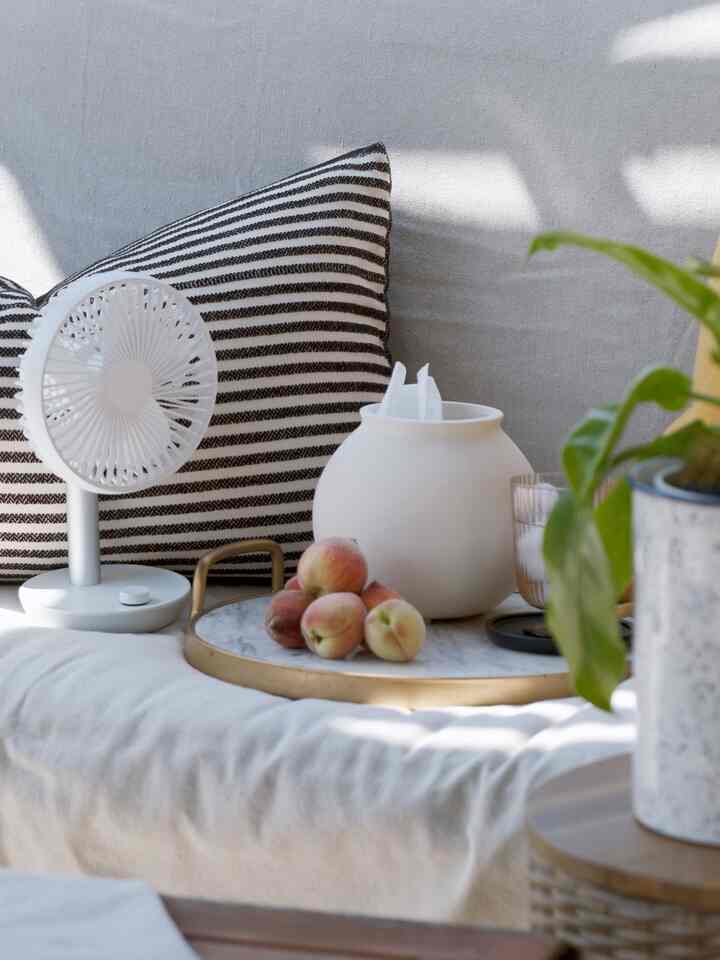White and beige sofa and cushions with fan, vase, and plants arranged in a cozy relaxation space