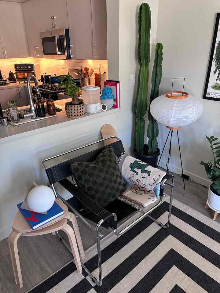 Natural-toned living room and kitchen featuring a modern armchair, stools, and a large cactus for a cozy atmosphere