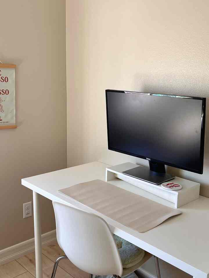 A white-toned home office space featuring a white desk and chair with a monitor on a monitor stand, creating a clean work environment