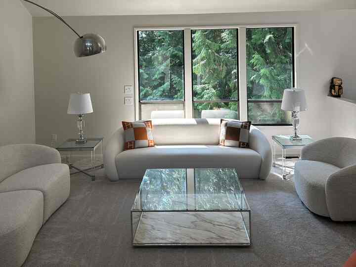 White-toned living room featuring a central sofa and glass coffee table, flanked by side tables and lamps, creating a modern atmosphere