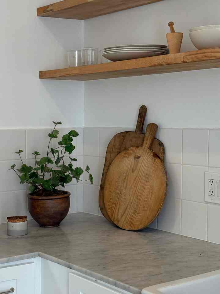 Bright kitchen corner with white tile walls, wooden shelves, and wooden cutting boards creating a cozy atmosphere