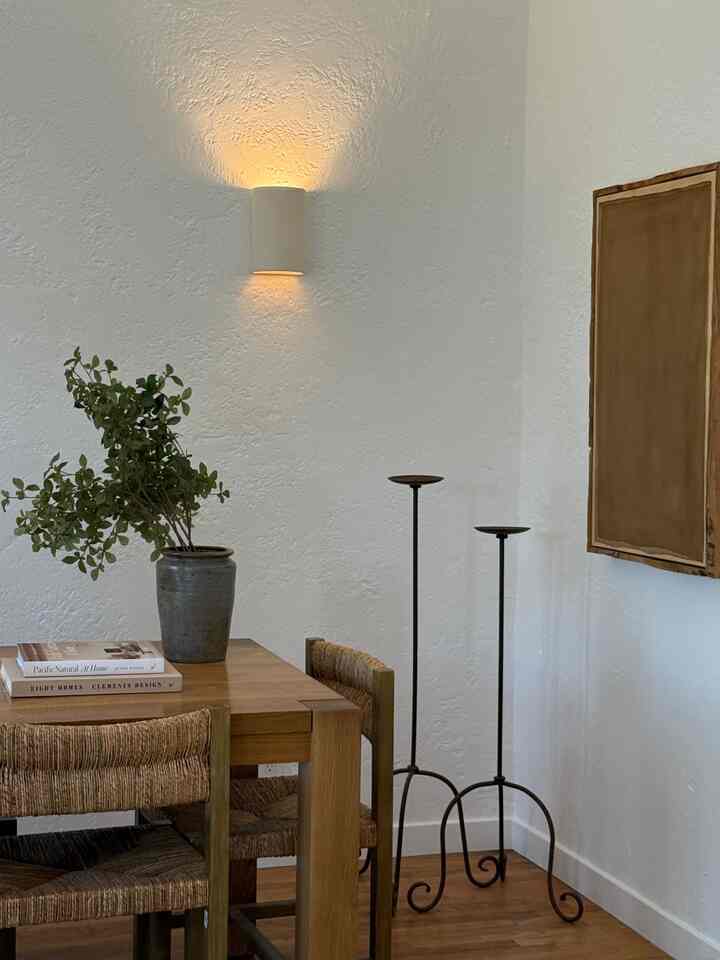 Wood tone and white dining room featuring wooden dining table with woven chairs, wall sconce, and iron candle holders creating a natural vintage atmosphere