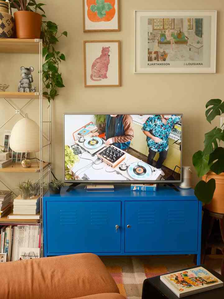 Beige-walled living room featuring a bright blue TV stand, sofa, shelves, and plants creating a natural atmosphere