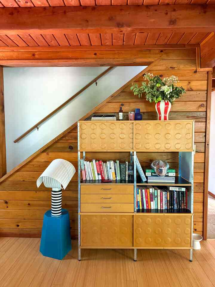Natural wood tone space under stairs featuring a storage unit with books and decorative items