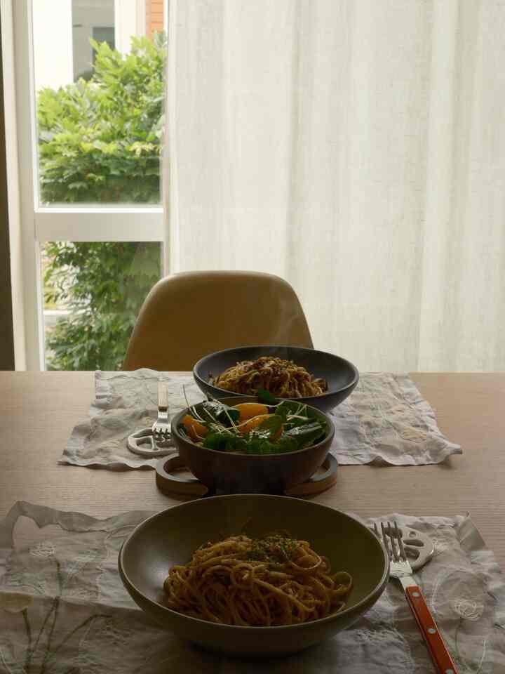 Beige-toned dining room featuring pasta plates, a salad bowl, and cutlery arranged on a wooden table with a natural atmosphere