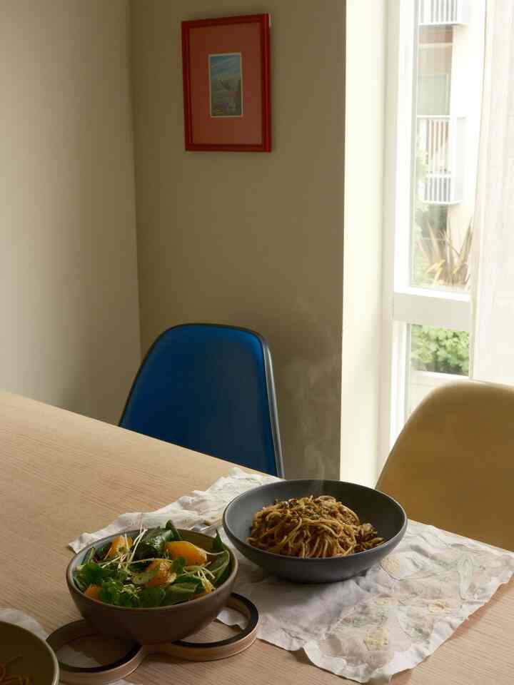 Beige-walled cozy dining space with a wooden table featuring steaming pasta and fresh salad bowls