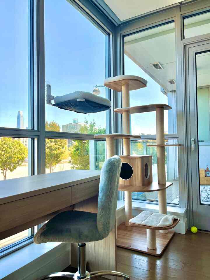 Wood-toned living room corner with abundant natural light featuring a desk and cat tower, creating a pet-friendly home office space