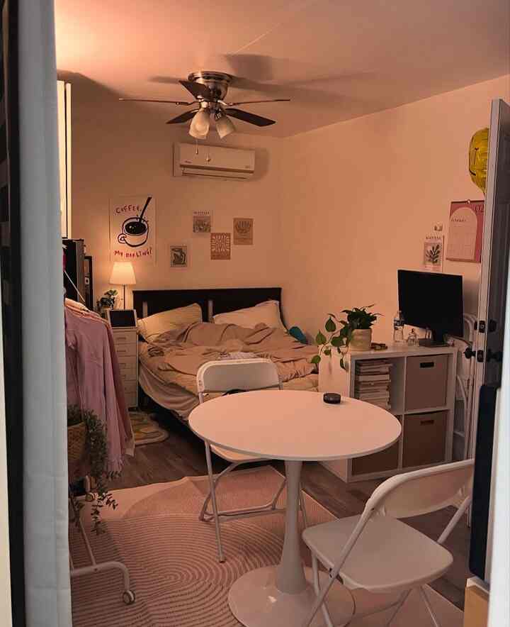 White and brown toned studio bedroom featuring a bed, round table, and desk with monitor in a cozy setting