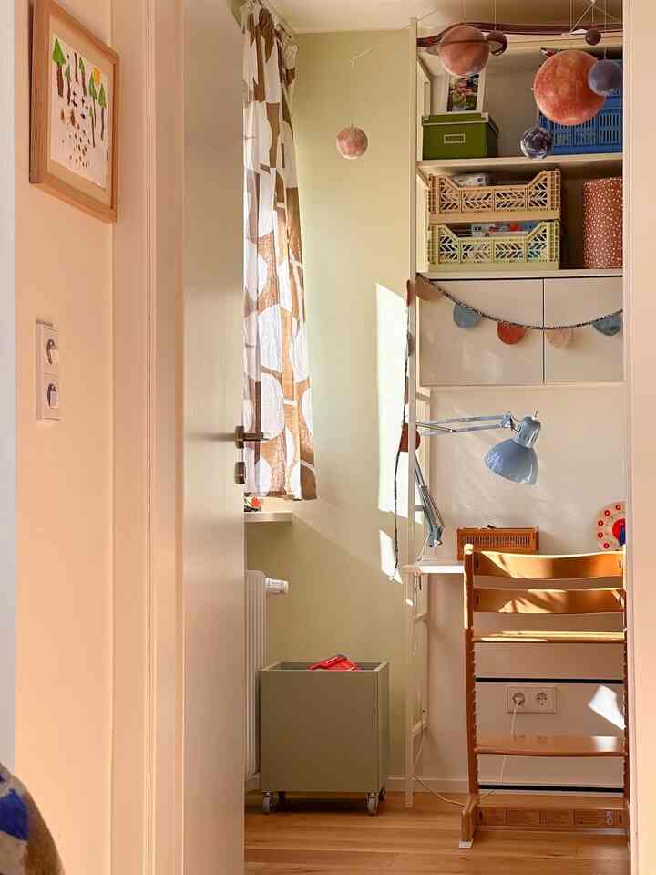Cozy kids' corner with warm beige and natural tones, featuring a child's desk and hanging planetary mobiles basked in sunlight