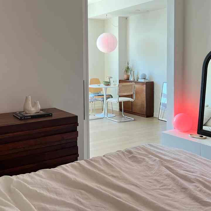 Minimal bedroom with white and brown tones featuring bed, side table, and a small dining nook with natural accents