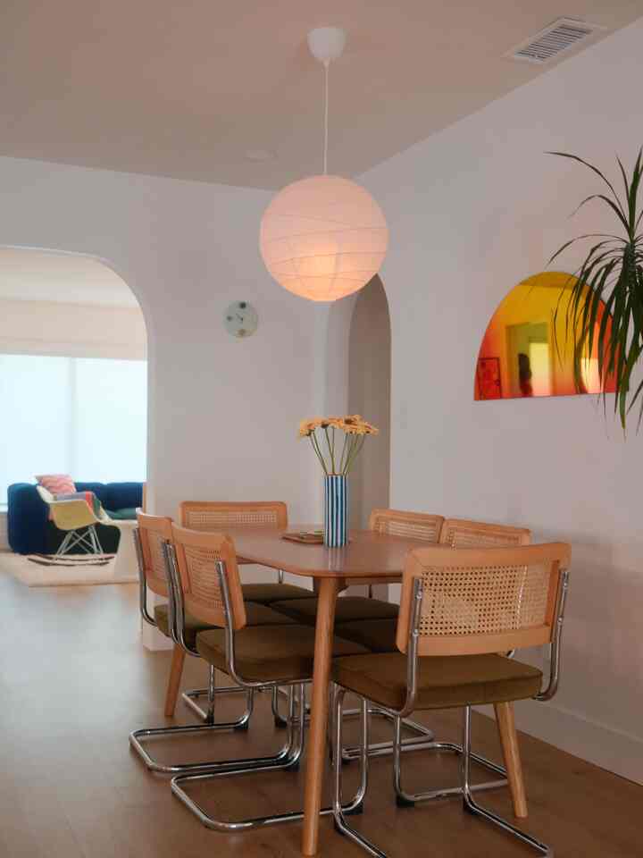 Soft wood tones and white walls define a dining room featuring a round pendant light and a vase with flowers, creating a cozy natural space