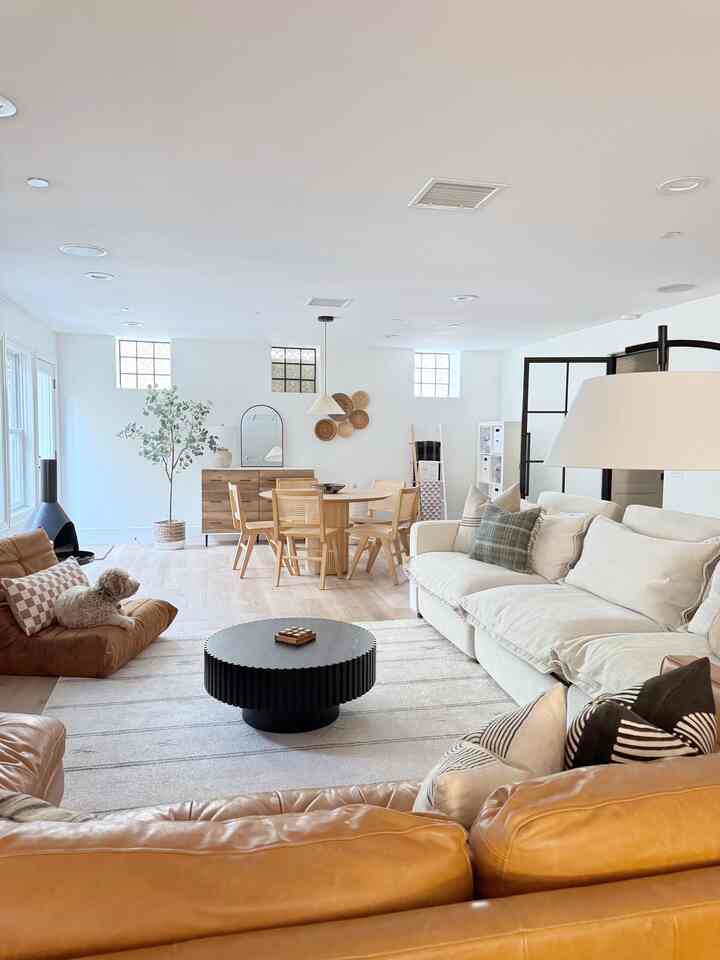 Bright white and natural beige toned living and dining room featuring beige leather bean bags, sofa, and wooden dining table with chairs in a cozy layout