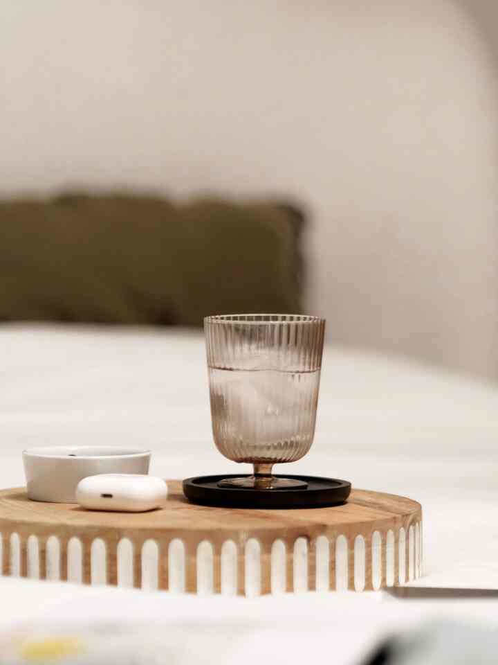 A white and wood-toned bedroom featuring a wooden tray with glass and AirPods, creating a serene atmosphere